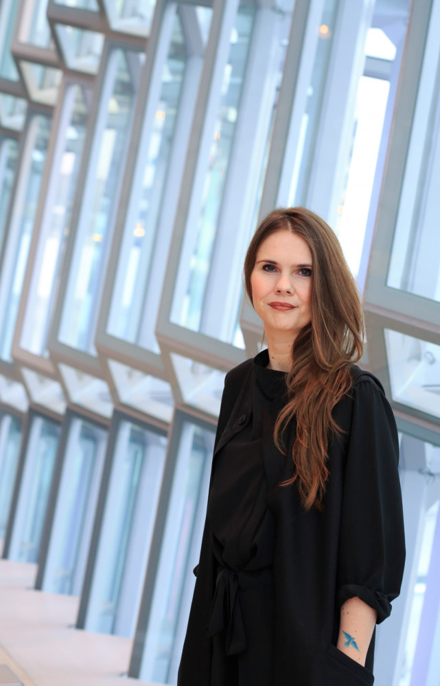 Sara Jónsdóttir, directrice du festival DesignMarch, pose ici devant les vitraux inclinés d’Harpa, tous d’une forme irrégulière...
