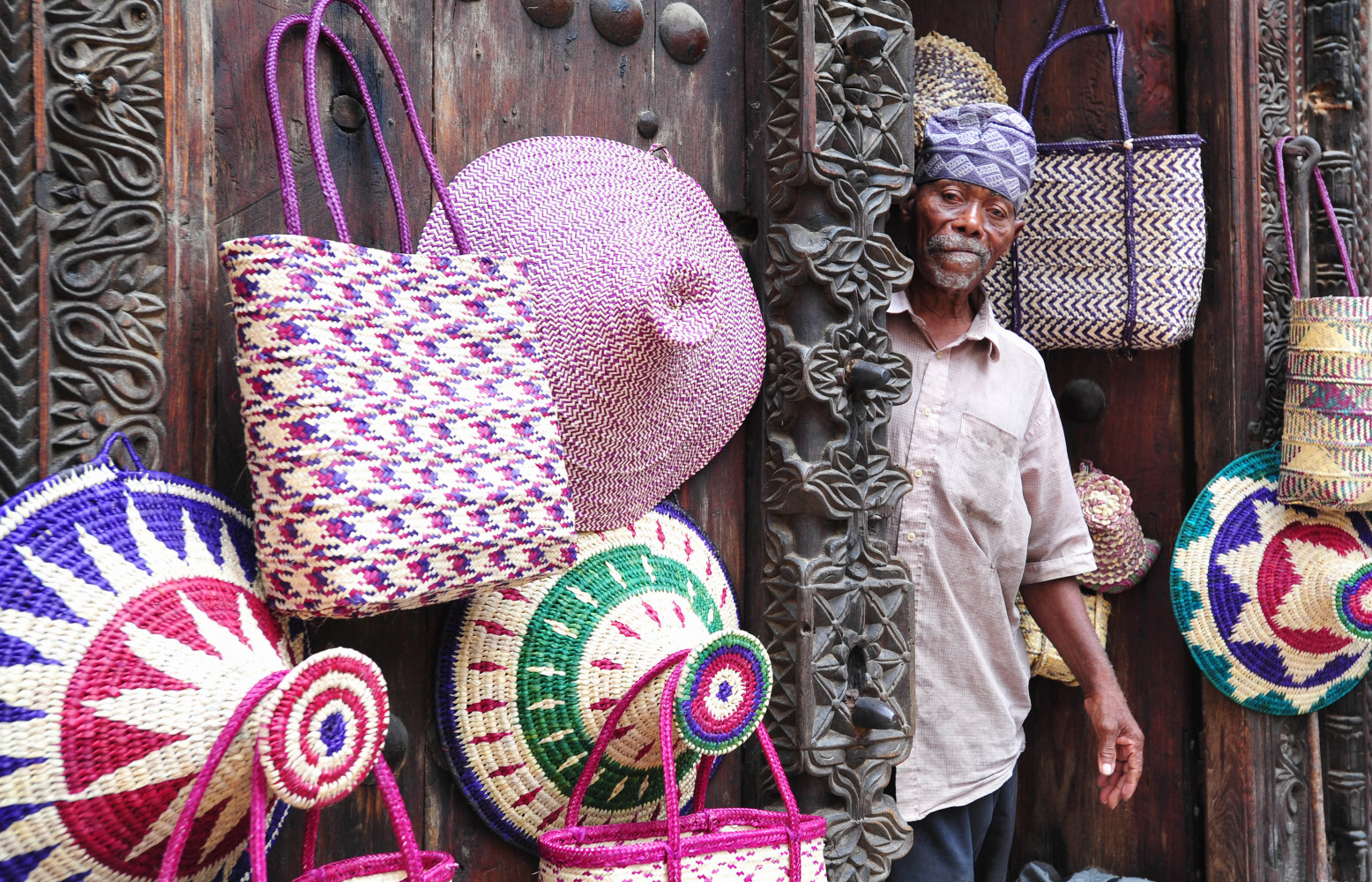 Vendeur de paniers derrière sa porte sculptée omanaise.