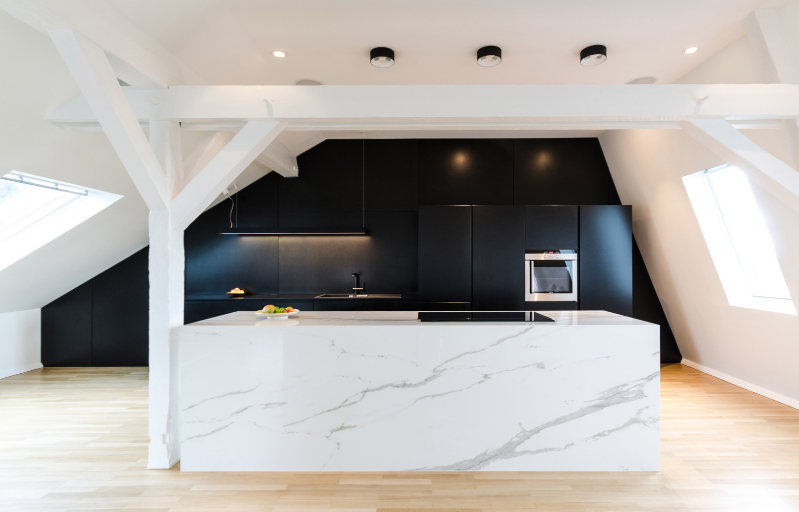 Dans la cuisine, dissociée de l'espace repas par un îlot en céramique, les rangements semblent disparaître grâce...