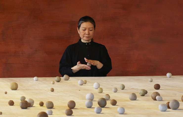 L’artiste Kimssoja, à table, en train de rouler de petites boules d’argiles. Installation « Archive of Mind » (2017).