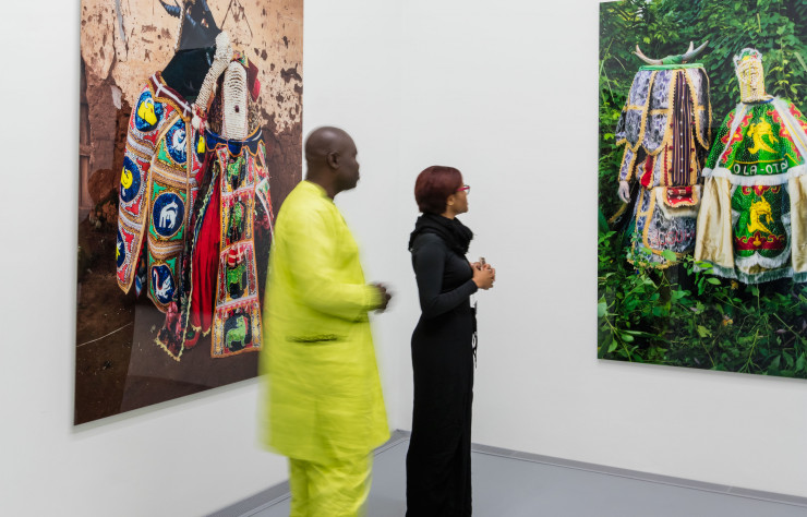 L’artiste Leonce Raphael Agbodjelou se tient devant deux de ses œuvres exposées pour l’accrochage inaugural du musée.