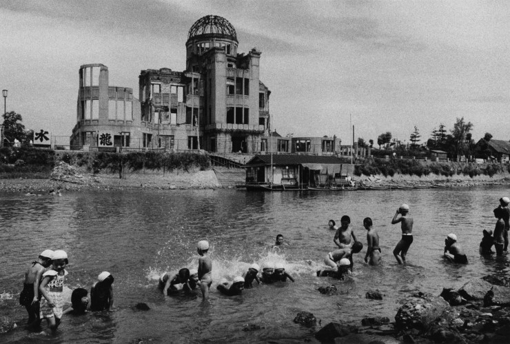 Cette composition d’un noir et blanc très contrasté rend compte d’une scène de jeux dans la rivière Motoyasu aux abords du Dôme de la bombe atomique d’Hiroshima.