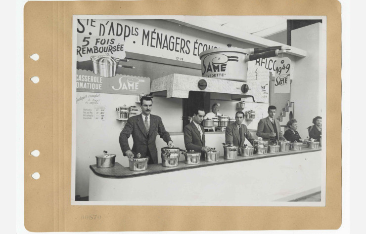 Cette photographie d’archive s’attarde sur un des nombreux stands du fameux Salon des Arts Ménagers. Ici, ce sont des démonstrateurs de casseroles automatiques au stand SAME (Société d’appareils ménagers Économiques) en 1949.