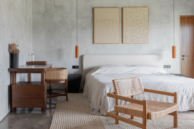 Dans la chambre parentale aux murs bruts, mobilier Le Bureau en teck recyclé, et L’Assise, en teck et en rotin naturel, table de nuit en bois de suar brûlé et fauteuil en teck et en rotin naturel (le tout, Kosame). Au-dessus du lit, œuvres Madstone&Co. Draps en bambou (Heveya). Tapis Rugs For Good.