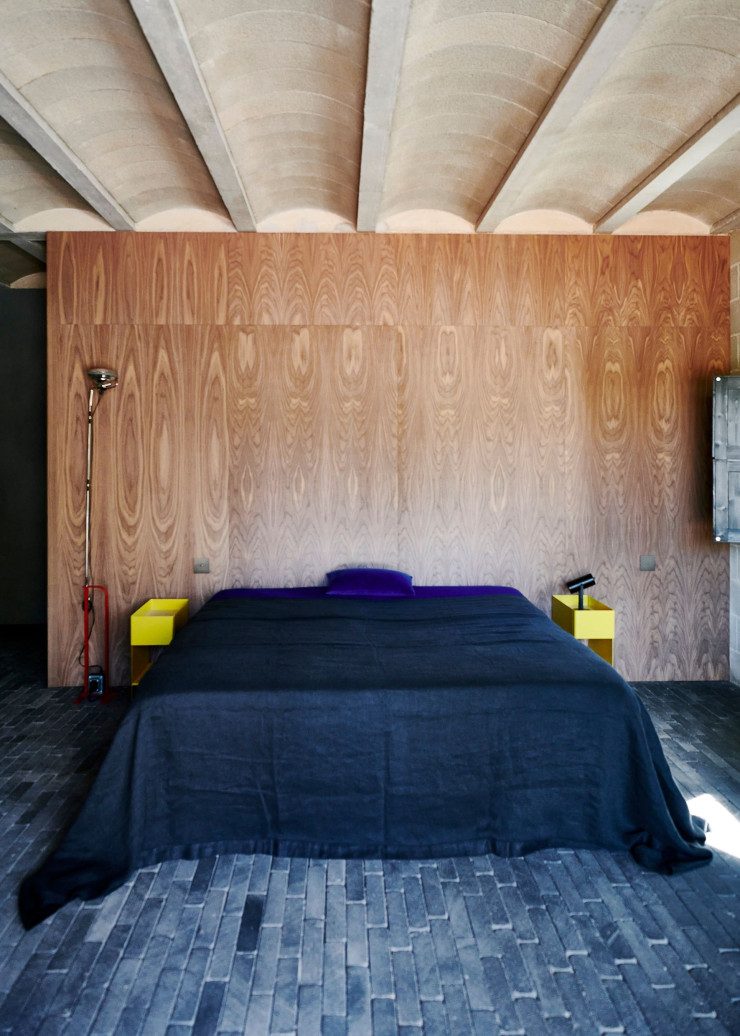 Dans la chambre principale, on retrouve le plafond et ses voûtes de béton ainsi que le sol en brique volcanique mexicaine, mais réchauffés ici par un panneau en bois. Lampadaire Toio d’Achille Castiglioni (Flos, 1962). Tables de chevet et lampe à poser vintage.