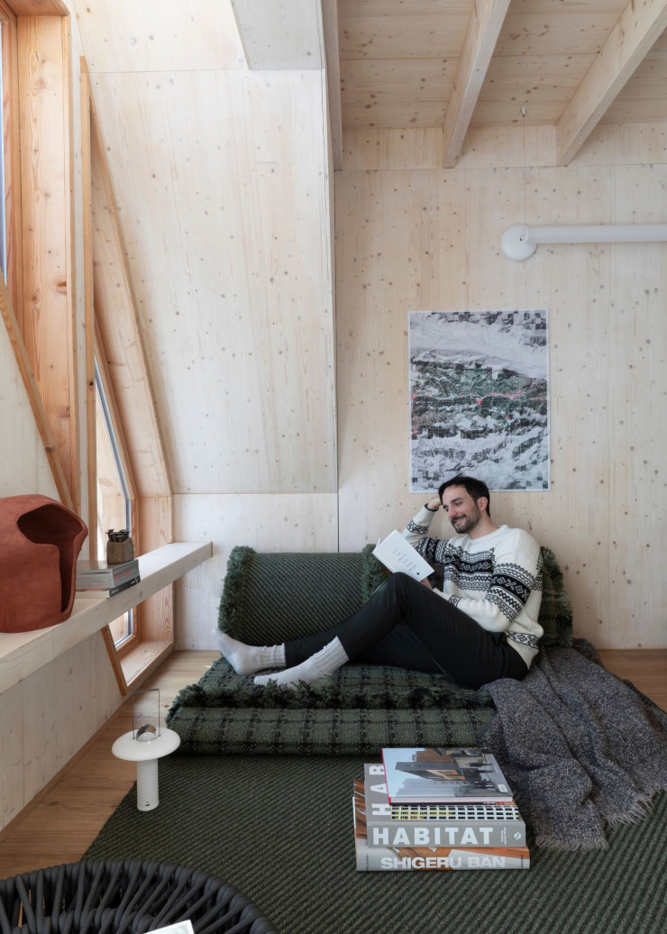 Dans l’espace repos habillé d’épicéa, l’architecte Luca Beltrame s’adonne à la lecture. Système d’assises comprenant coussins et tapis Garden Layers, de Patricia Urquiola (GAN). Couverture en cachemire Society Limonta. Lampe à poser Camping (Linea Light). Sur l’étagère, céramique de la collection « Nostalghia/Nido », de Daniela Daz Moretti Studio. Au mur, œuvre de Luca Beltrame.