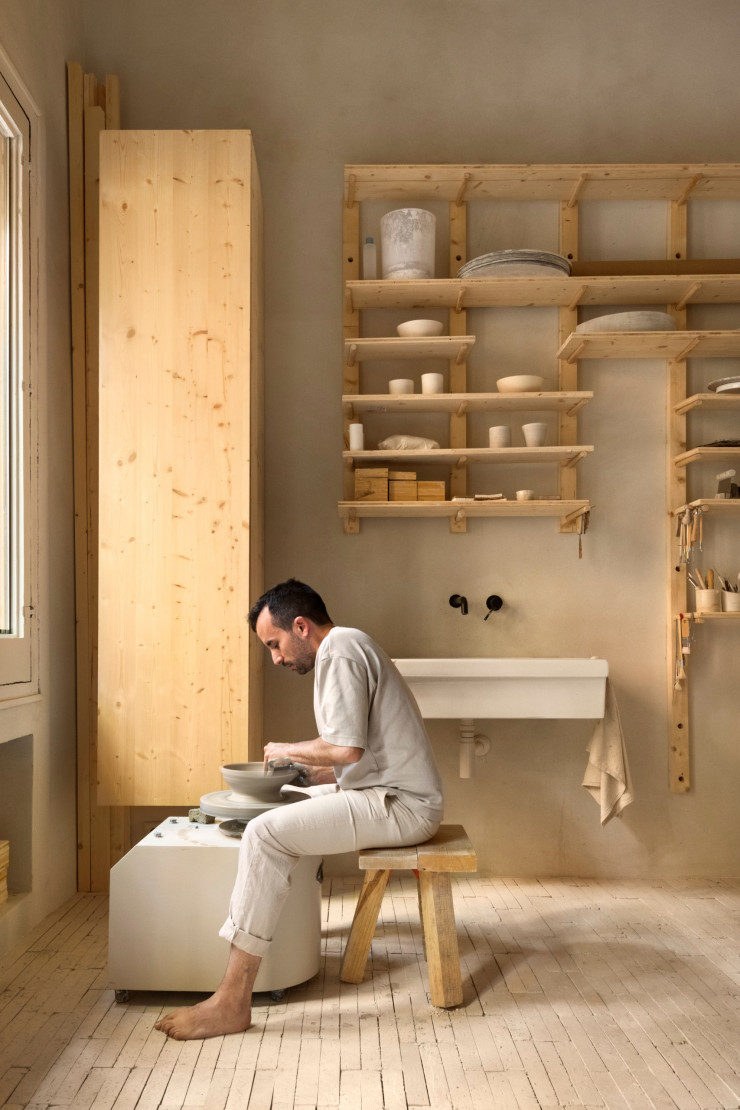 Dans son atelier, Alberto Aranda tourne une céramique assis sur le tabouret en bois « La pieza » T300, de Curro Claret.
